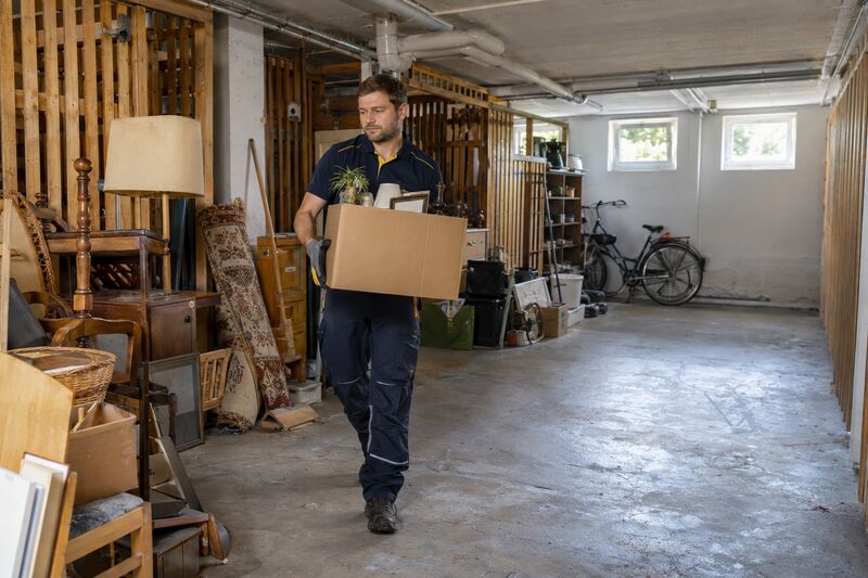 Mitarbeiter trägt einen Karton aus einem vollen Kellerraum